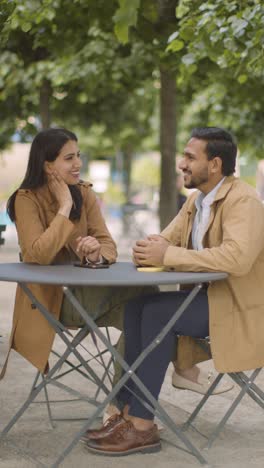 Video-Vertical-De-Una-Pareja-Musulmana-En-Una-Cita-Sentada-En-Una-Mesa-Al-Aire-Libre-En-Una-Calle-De-La-Ciudad-Hablando-Juntos